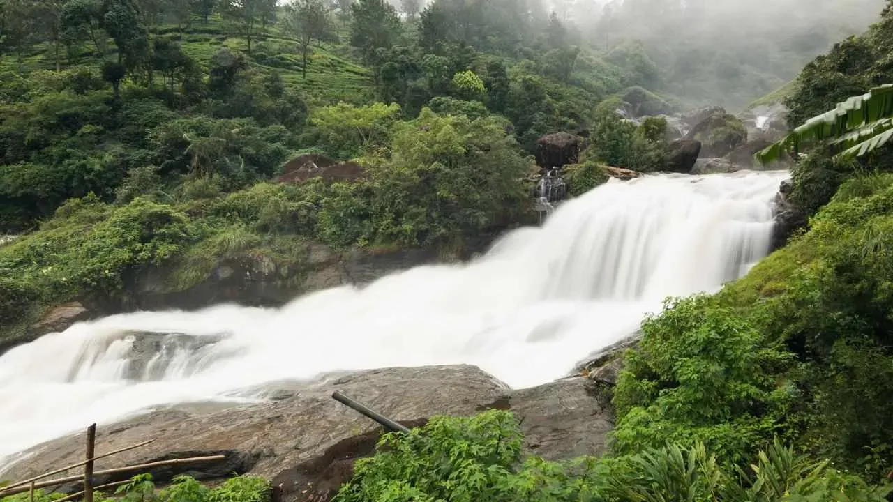 Waters of Attukad Waterfalls rolling through the rocks amidst green forest.